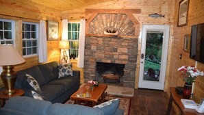 A cozy cabin interior with a stone fireplace, wooden walls, a sofa, and a coffee table. - Waterfall Cottage within sight & sound of Cane Creek Falls, 2BR 2BA (Dahlonega)