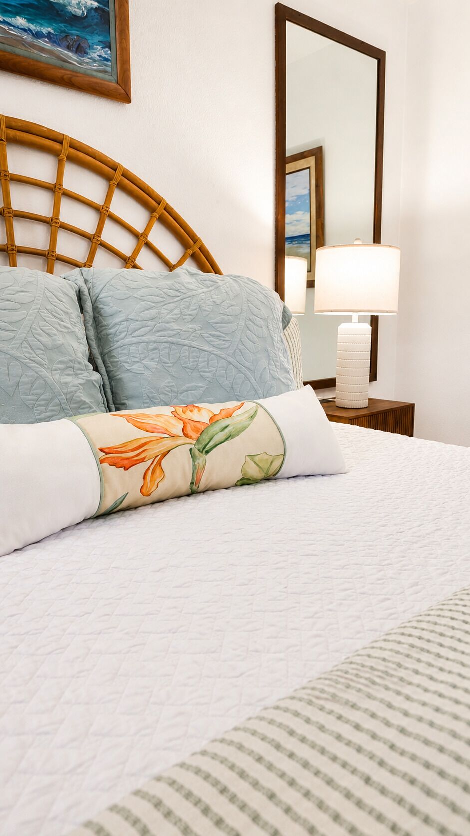A neatly made bed with a floral pillow, a bedside lamp, and a framed picture on the wall.