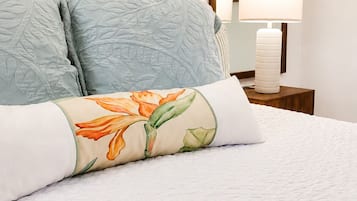 A neatly made bed with a floral pillow, a bedside lamp, and a framed picture on the wall.