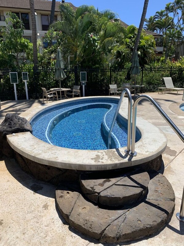 A swimming pool with a tiled edge, surrounded by lounge chairs and palm trees. - An Affordable Alternative to Expensive Accommodations in Poipu (Koloa)