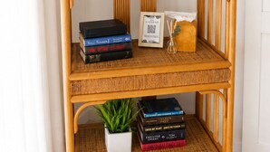 A rattan TV stand with a flat-screen TV, books, a small plant, and a framed picture. - An Affordable Alternative to Expensive Accommodations in Poipu (Koloa)