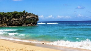 A beach with clear turquoise water, a sandy shore, and a rocky outcrop with vegetation. - An Affordable Alternative to Expensive Accommodations in Poipu (Koloa)