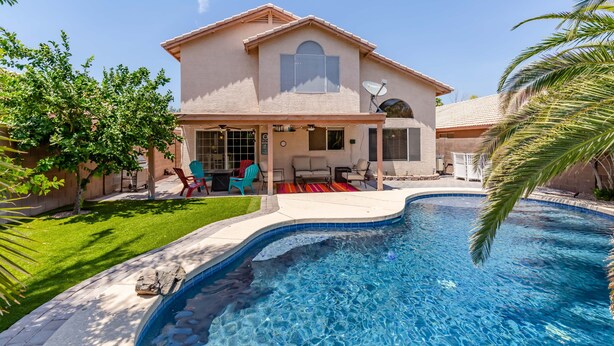 A house with a swimming pool, a patio with chairs, and a satellite dish.