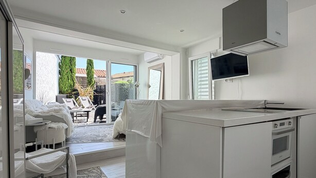 A modern kitchen with a central island, built-in oven, and a large window overlooking a patio area. - MAISON LITTLE WHITE HOUSE (Anglet)