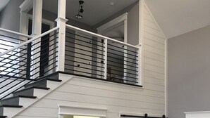 Un intérieur spacieux avec un escalier menant à un niveau supérieur, un coin repas avec des tabourets et un meuble blanc avec des tiroirs.