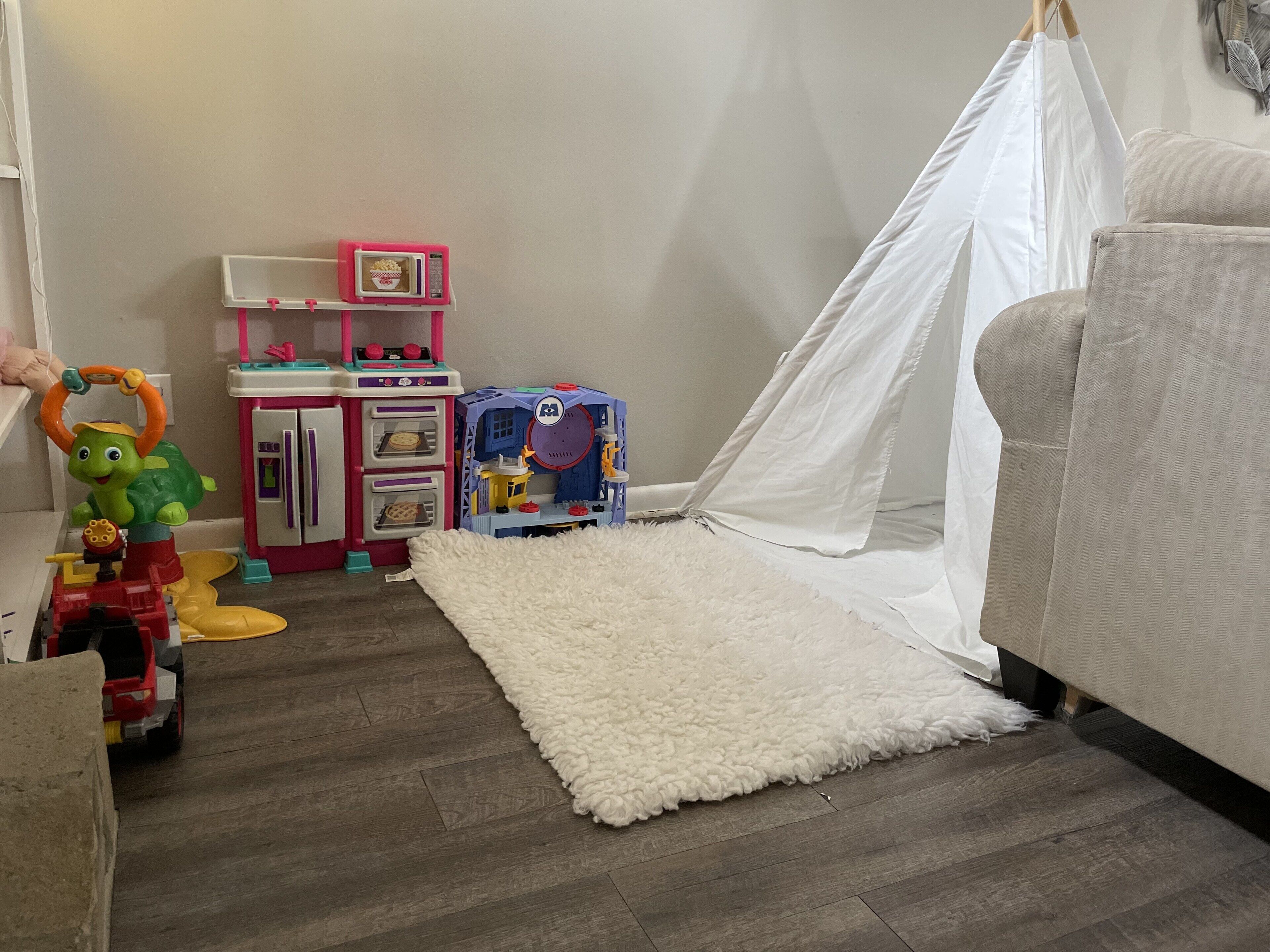 Una habitación con un manto blanco mullido, una tienda de campaña blanca, un juego de cocina rosa y un vehículo de juguete.