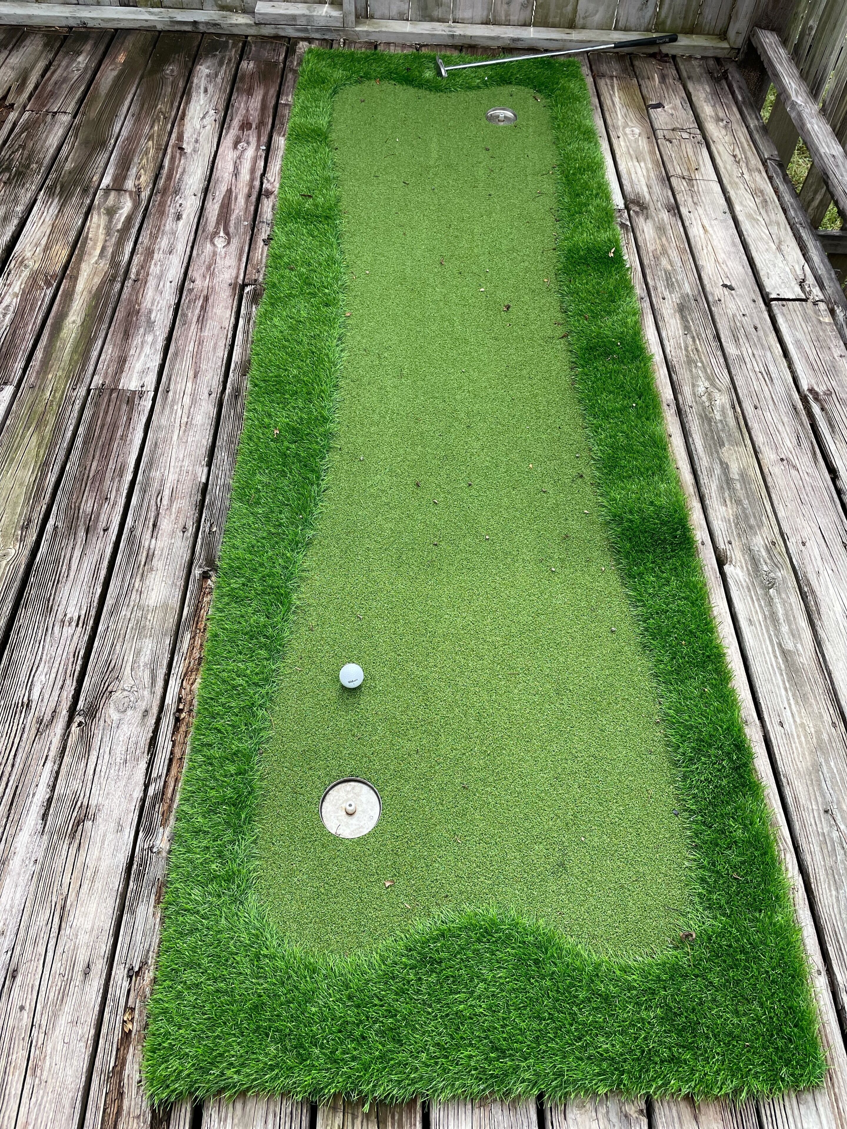 Un área rectangular de césped artificial con dos pelotas de golf y una placa de metal, rodeada de tablones de madera.