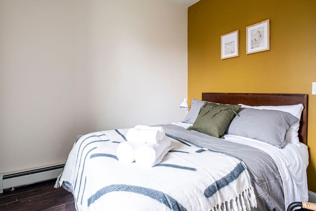 Een netjes opgemaakt bed met een gestreept deken, een houten hoofdbord en twee ingelijste foto's aan de muur.