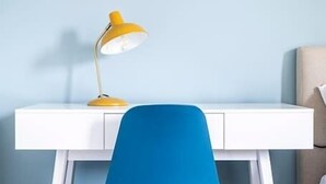 Un escritorio blanco con una lámpara de escritorio amarilla y una silla azul.