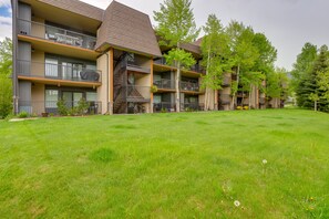 Un immeuble résidentiel à plusieurs étages, doté de balcons, d’une pelouse verdoyante et d’arbres.