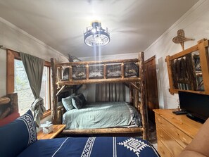 A bunk bed with a wooden frame, a television on a wooden dresser, and a window with curtains.