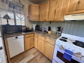 A compact kitchen with wooden cabinets, a Bosch dishwasher, a microwave, a stove, and a window with blinds.