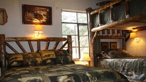 A rustic room with a large bed featuring a quilt with wildlife prints, a wooden headboard, and a bunk bed with a similar design. - Close to Downtown Estes Park, RMNP, Hot Tub, Activity Shed! Far View Cabin (Estes Park)