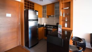 A modern kitchen with a stainless steel refrigerator, a gas stove, and wooden cabinets. - Apoquindo Green (Santiago)