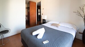 A hotel room with a bed, a chair, a lamp, and a door leading to a closet. - Apoquindo Green (Santiago)