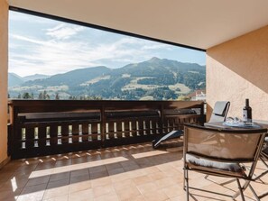 Ein Balkon mit einer hölzernen Bank, einem Tisch mit Stuhl und einer Weinflasche.