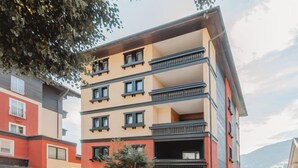 A multi-story building with balconies, a parking area, and a small tree in the foreground.
