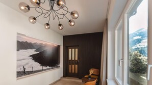 A modern interior with a large window, a painting of a mountainous landscape, and a dining area with a yellow chair.