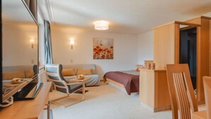 A modern hotel room with a bed, a desk, a chair, a sofa, and a painting on the wall.