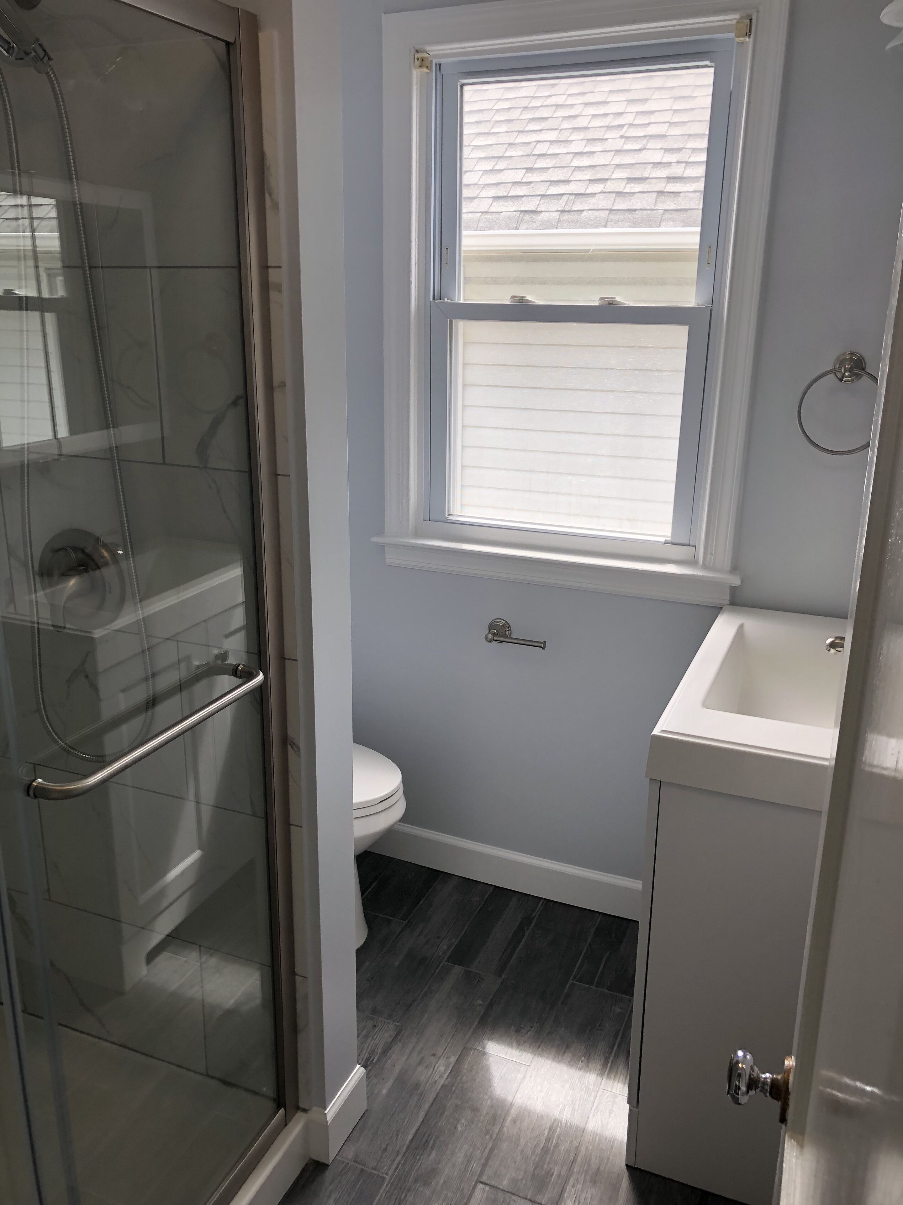 A bathroom with a glass shower enclosure, a toilet, a window, and a sink.