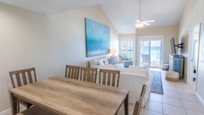 A dining area with a wooden table and chairs, a white sofa, and a view of the ocean through a sliding glass door. - Gulf Front, 3 Bedroom Condo, Small Complex, Dune Allen Beach, Santa Rosa Beach (Santa Rosa Beach)