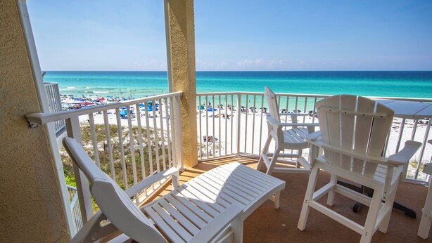A balcony with white chairs and a table, overlooking a beach with people and umbrellas. - Gulf Front, 3 Bedroom Condo, Small Complex, Dune Allen Beach, Santa Rosa Beach (Santa Rosa Beach)