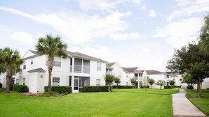 A row of white two-story townhouses with a well-maintained lawn and a sidewalk leading to the entrance.