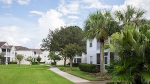 A residential area with a well-maintained lawn, a concrete pathway, and houses with white exteriors and dark roofs.