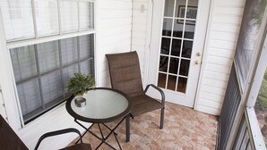 A small patio area with a table and two chairs, a potted plant, and a white door with glass panels.