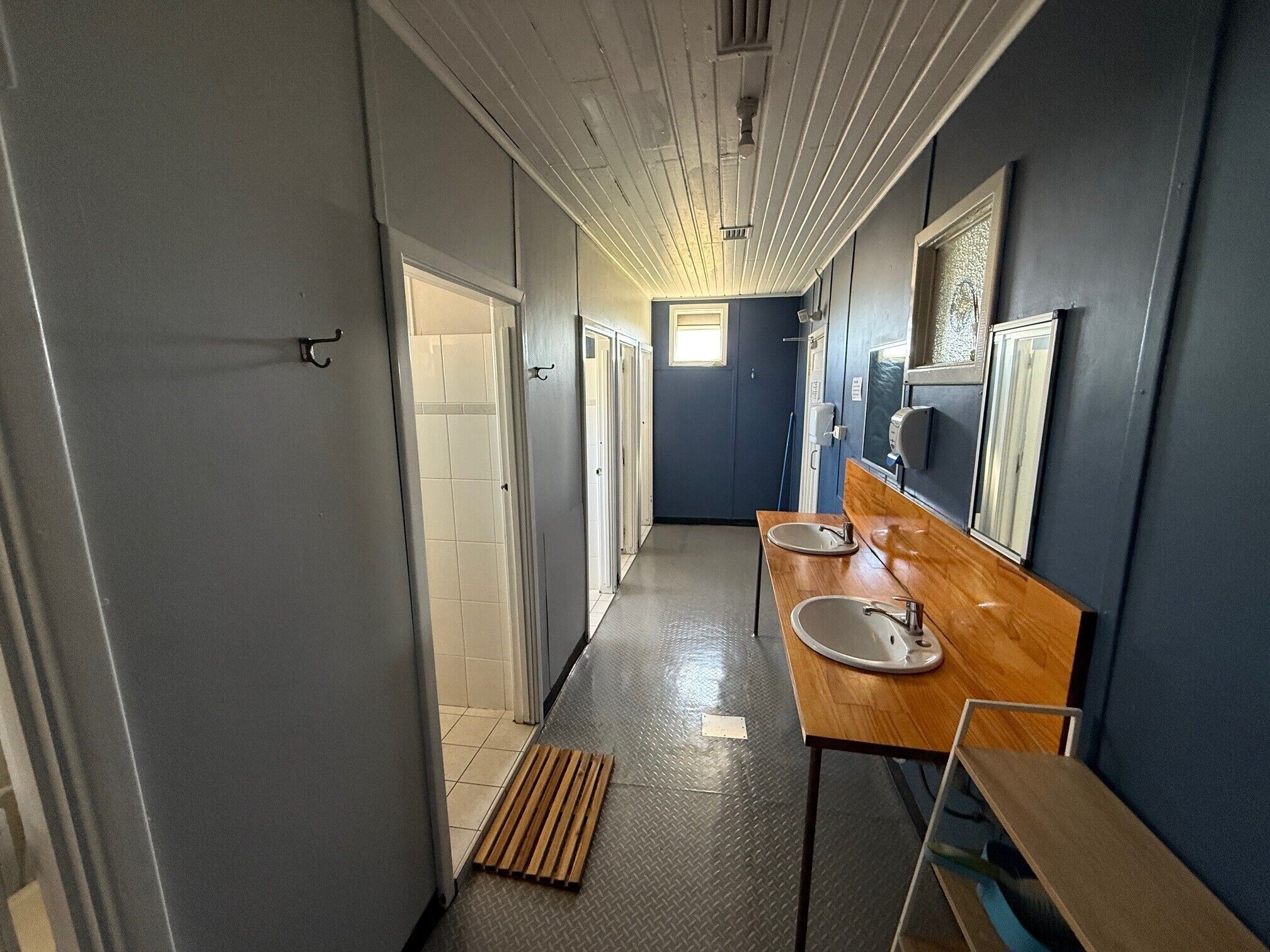 A narrow hallway with a wooden bench, a sink, and a mirror.