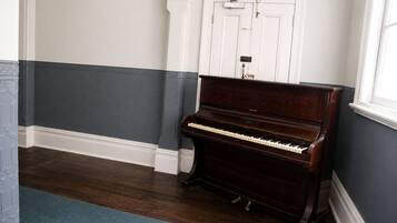 A piano in a room with a dark wooden floor, white and dark blue walls, and a white door in the background.