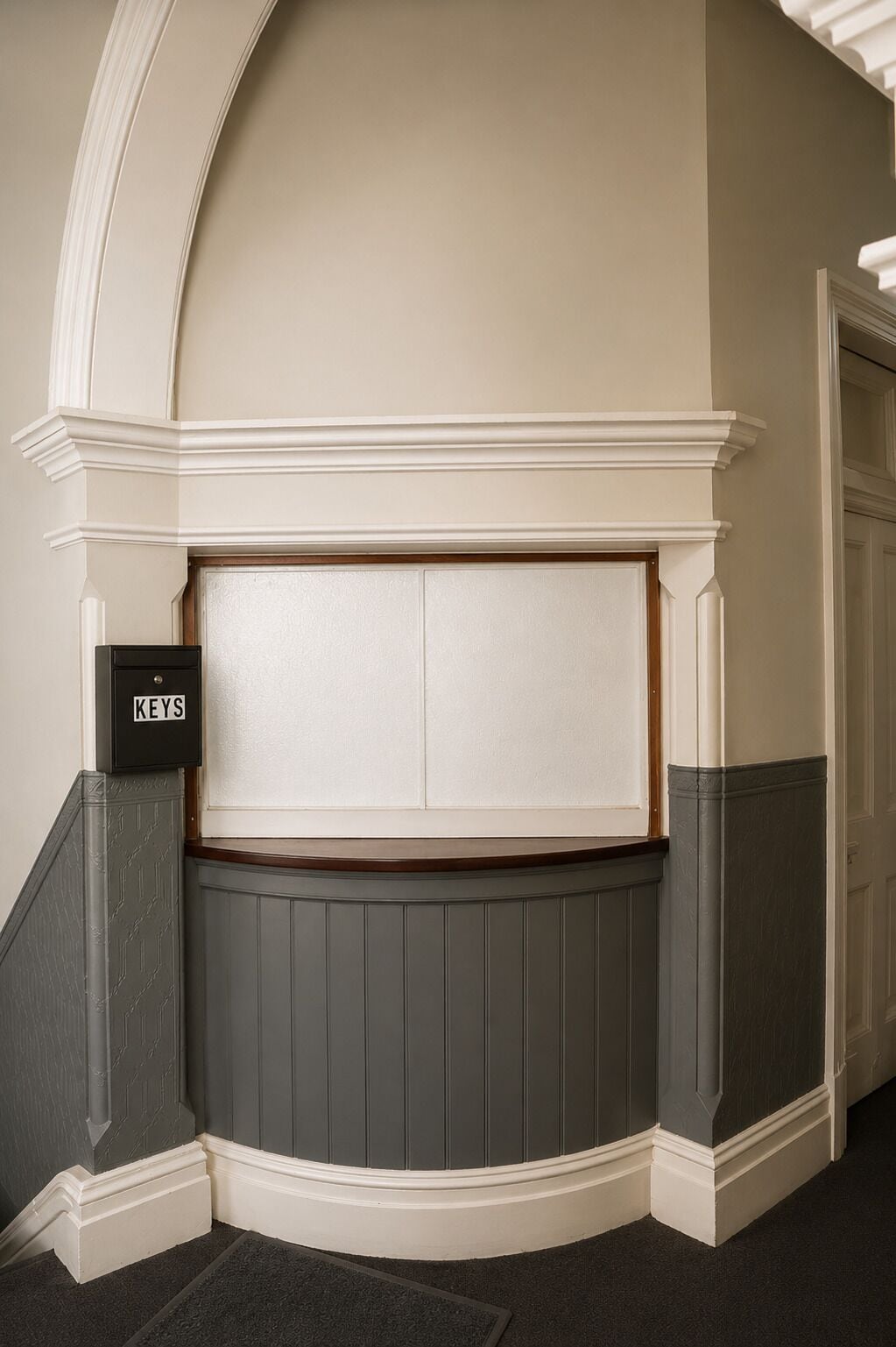 A corner of a room with a white wall, a grey wainscotted wall, and a door with a white frame.