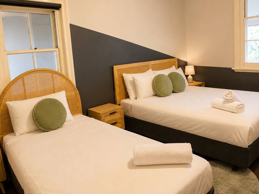 Ein Hotelzimmer mit zwei Betten, jeweils mit Holz Kopfteil, weißer Bettwäsche und einem grünen Kopfkissen. Es gibt Nachttische mit Lampen und ein Fenster mit Blick.
