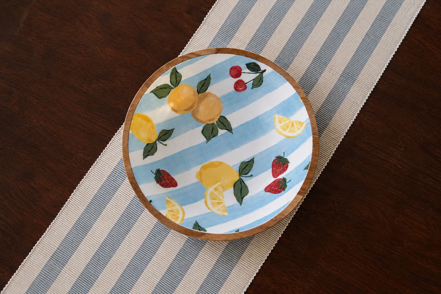 A round table with a striped tablecloth and a plate with fruit illustrations.