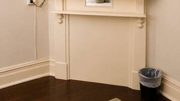 A television mounted on a white wall with a small shelf below it, a lamp to the left, and a trash can to the right.