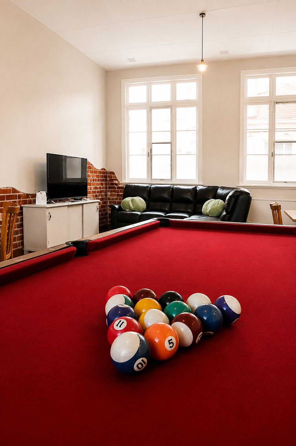 A pool table with balls, a television, a sofa, and windows.