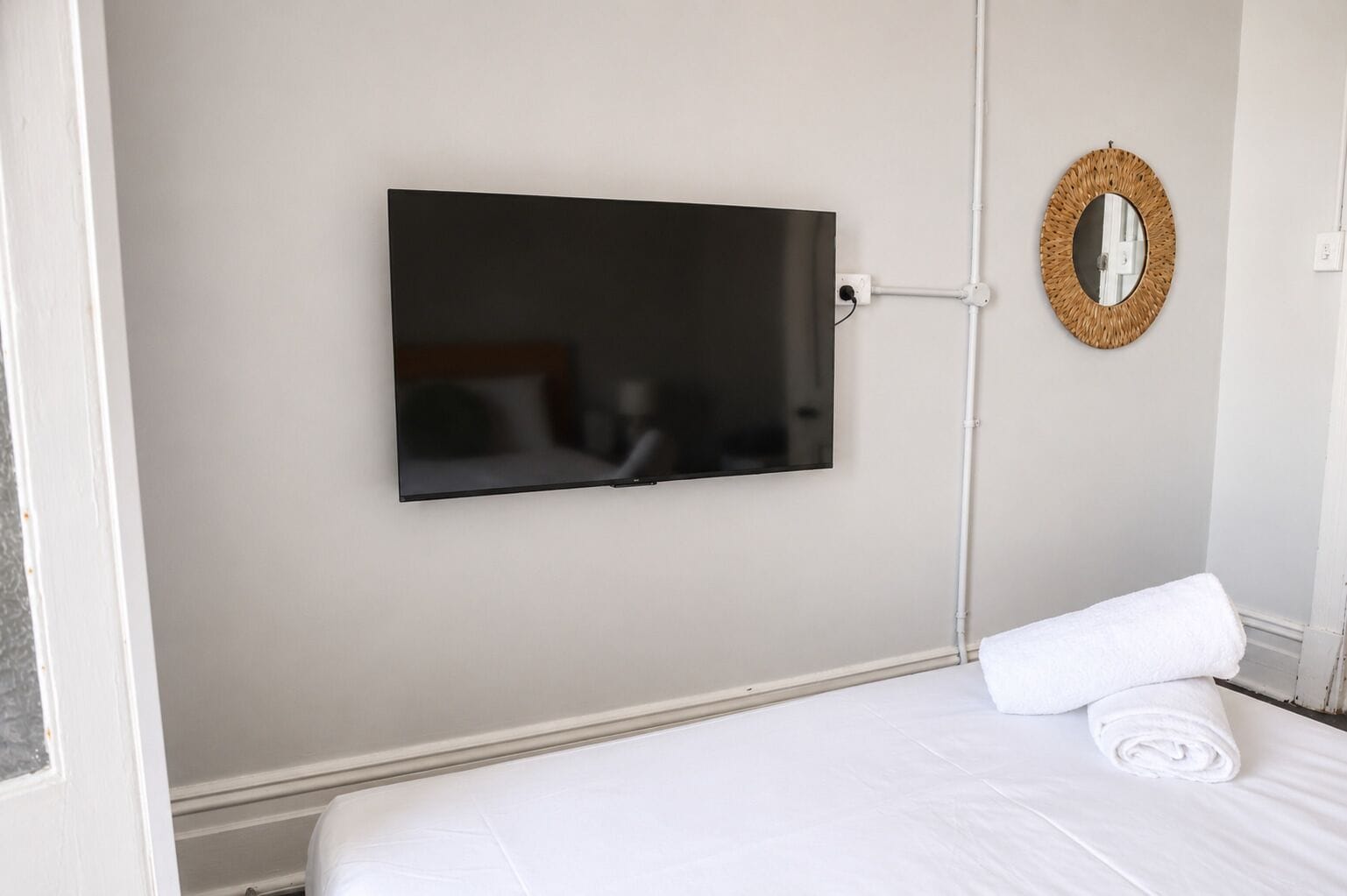 Ett hotellrum med en säng, en platt-TV som är monterad på väggen och en vit handduk på sängen.