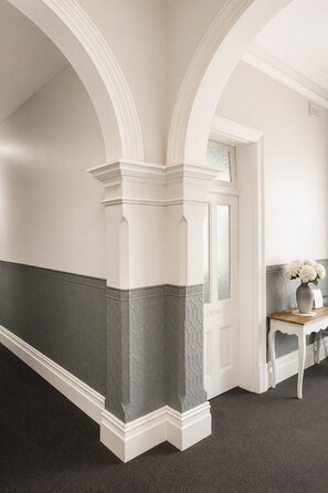 A hallway with white and grey wainscoting, a door labeled 'Lounge', and a table with a vase of flowers. - Shoreline Lodge Geraldton (Geraldton)