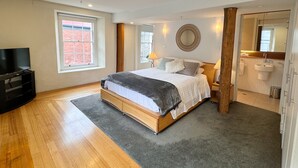 Een slaapkamer met een bed, een televisie, een raam en een badkamer die door een geopende deur zichtbaar is.
