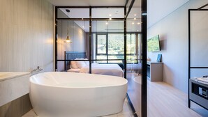 A modern bathroom with a large bathtub, a separate shower area, and a view of a balcony with a bed.