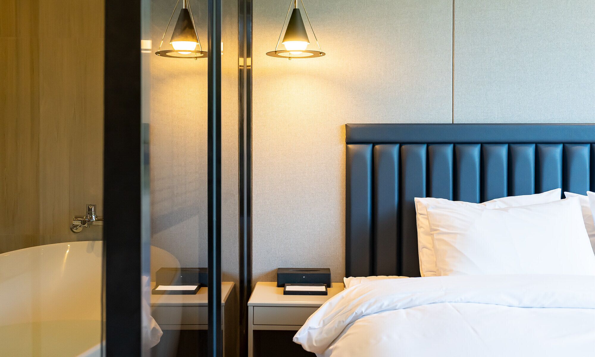 A modern hotel room with a large bed, a nightstand, a reading lamp, and a bathtub.