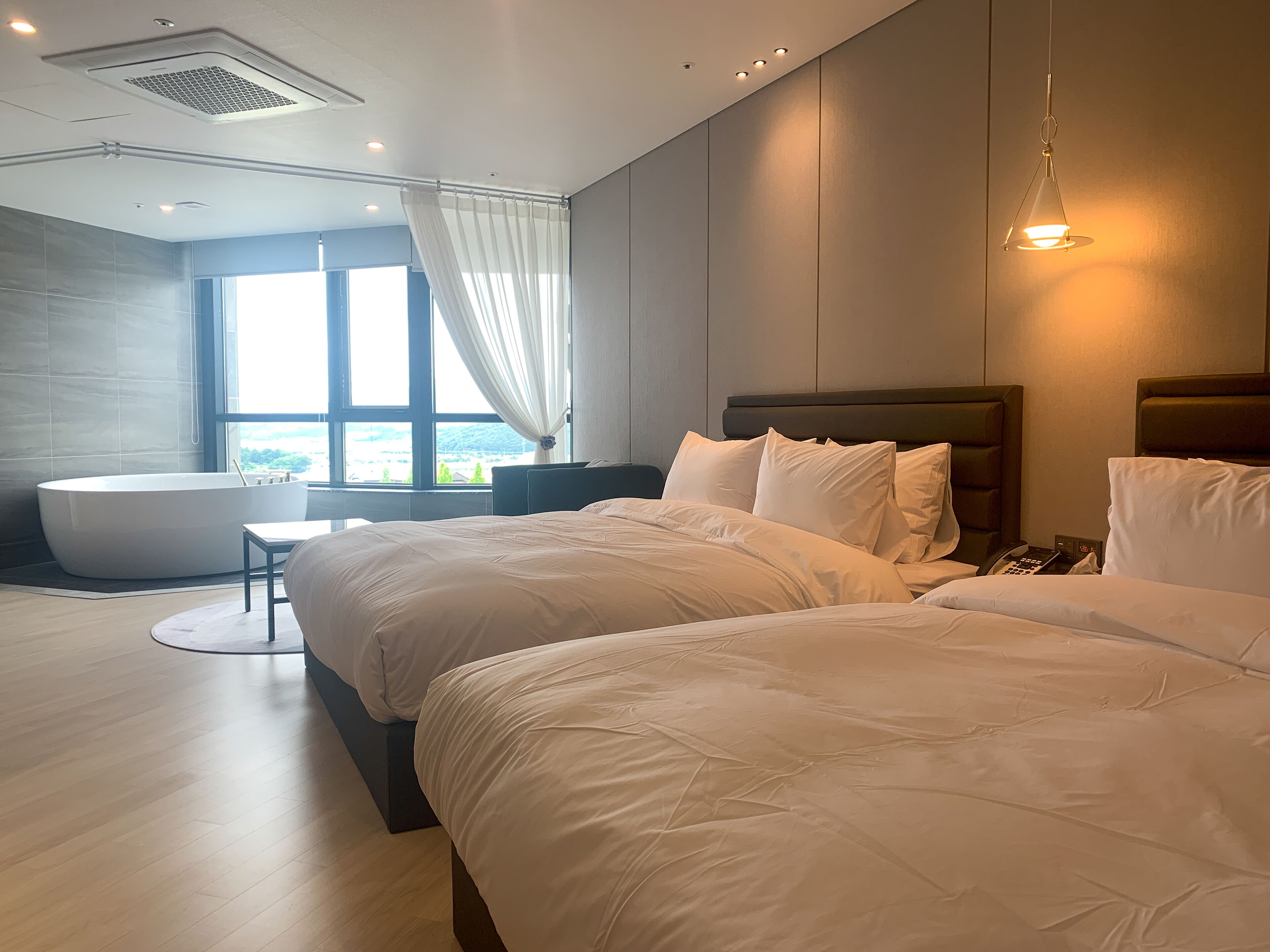 A modern hotel room with a large bed, a separate seating area, a bathtub, and a view of the outdoors.