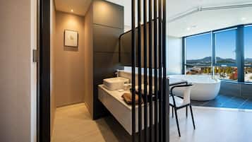 Un baño moderno con bañera, un espejo grande y vistas a la ciudad a través de amplias ventanas.