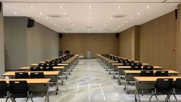 A conference room with rows of tables and chairs, a marble floor, and a high ceiling with recessed lighting.