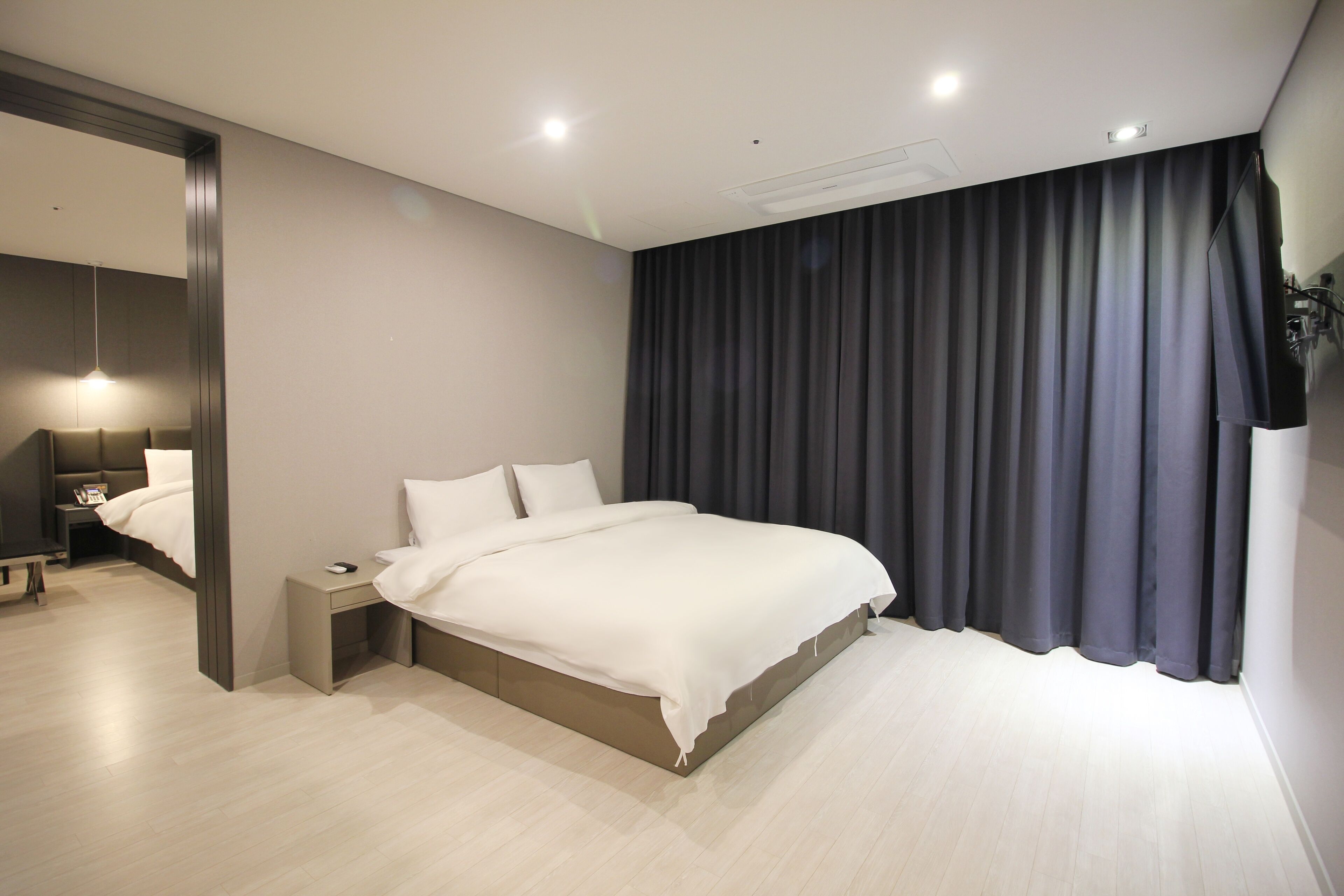 Un dormitorio moderno con una cama grande, mesitas de noche, un espejo y una cortina oscura.