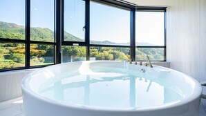 A large, white bathtub in a room with large windows overlooking a mountainous landscape.