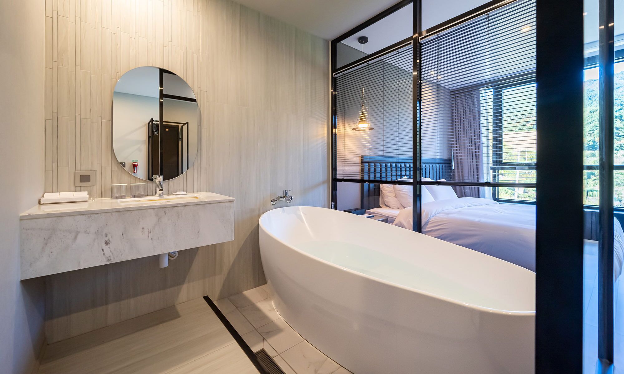 A modern bathroom with a freestanding bathtub, a large mirror, and a window with blinds.