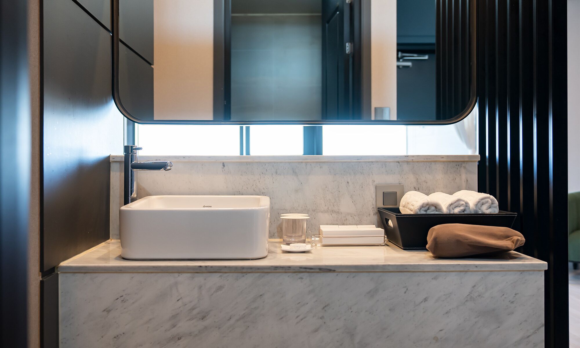 Un baño moderno con un espejo grande, un lavamanos blanco y una encimera de mármol.