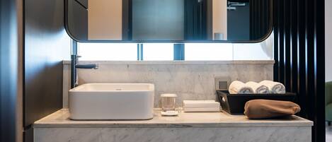 Un baño moderno con un espejo grande, un lavamanos blanco y una encimera de mármol.
