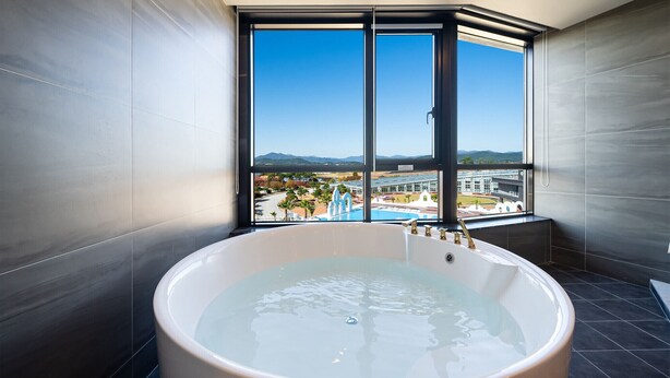 A modern bathroom with a large bathtub, a view of a resort, and a large window.
